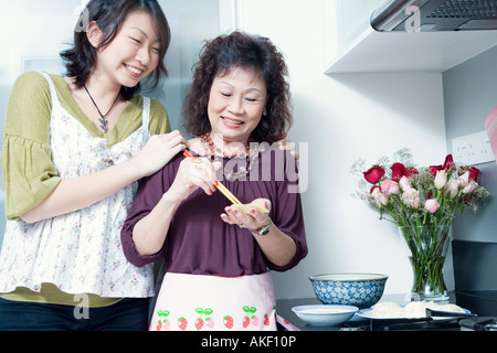 Senior woman preparing food with her granddaughter standing behind her and smiling Stock Photo