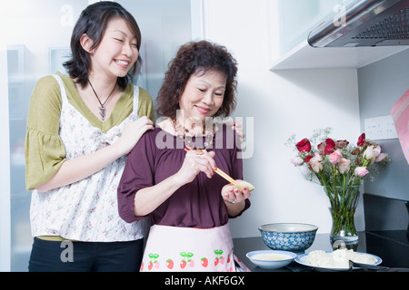 Senior woman preparing food with her granddaughter standing behind her and smiling Stock Photo