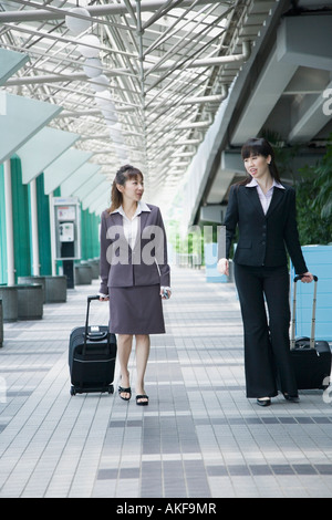 Two businesswomen walking on a walkway with their luggage