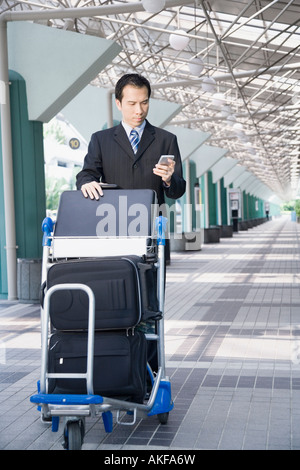 Businessman using a palmtop and pushing a luggage cart Stock Photo