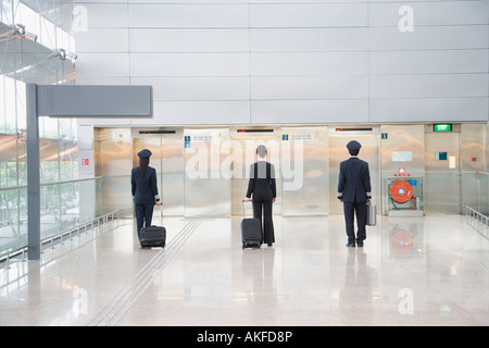 Rear view of a male and a female pilot walking with a female cabin crew in front of elevators Stock Photo