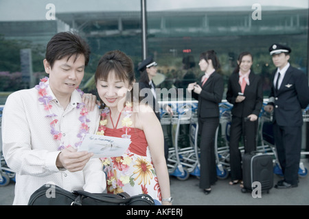 Mature couple looking at an airplane ticket with pilots and cabin crews standing in the background Stock Photo