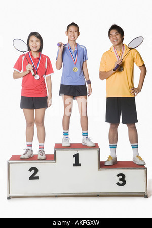 Portrait of two young women and a young man standing on a winners podium and wearing sports medal Stock Photo