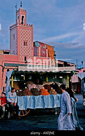Stall selling fruit and nuts in Djemma el Fna Marrakesh Morocco kasbah mosque in background couple in local dress walking past Stock Photo