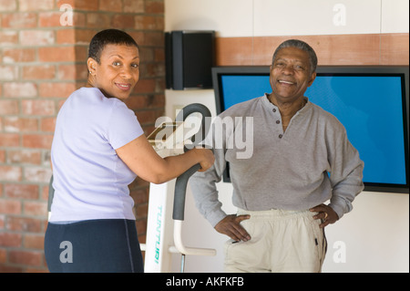 Seniors African Americans Exercising on stepper machine and plasma TV Stock Photo