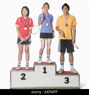 Portrait of two young women and a young man standing on a winners podium and wearing sports medal Stock Photo