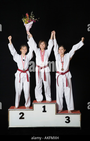 Three young women raising their hands on a winners podium Stock Photo