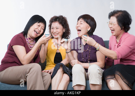 Three senior women and a mature woman holding tea cups and laughing Stock Photo