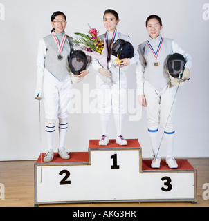 Portrait of three young women in fencing costumes standing on a winner's podium Stock Photo