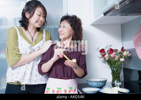 Senior woman preparing food with her granddaughter standing behind her and smiling Stock Photo