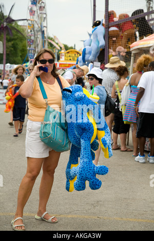 WISCONSIN Milwaukee Adult woman talk on cellular phone hold giant stuffed blue frog near amusement rides Stock Photo