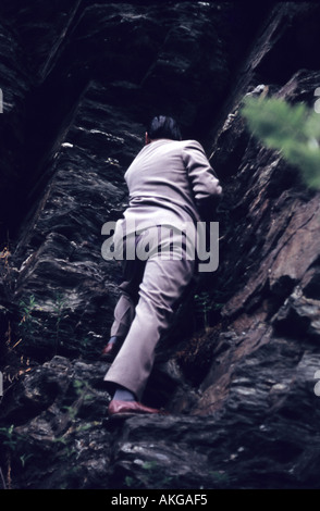 a man in business suit climbing a rock 1965 Germany Stock Photo