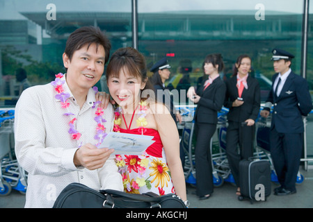 Mature couple looking at an airplane ticket with pilots and cabin crews standing in the background Stock Photo