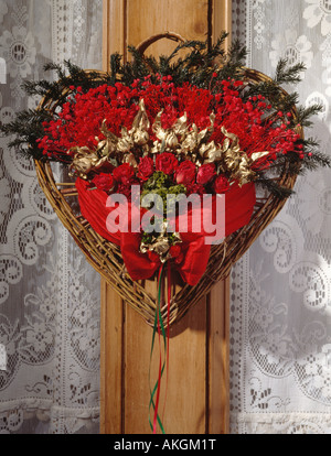 Close- up of heart shaped Christmas decoration with dried red roses and gold seed-heads wrapped with red ribbon Stock Photo