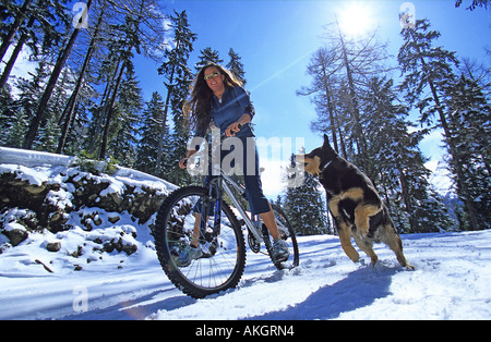 Women mountain bikes down a snowy track in the French Alps with her dog Stock Photo