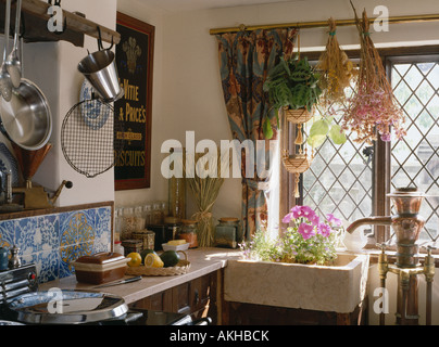 Dried flowers hanging above ceramic sink below lattice window in cottage kitchen Stock Photo