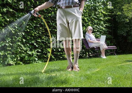 Man watering lawn and woman using laptop Stock Photo