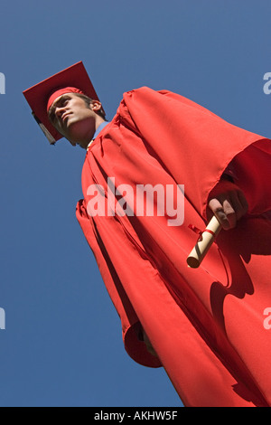 A proud graduate in red cap and gown holding his diploma and looking toward the future Stock Photo