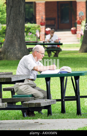 Male retiree sitting on at a park bench reading his book Stock Photo