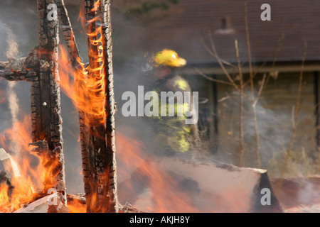 A firefighter in a yellow helmet is walking around the remains of a structure fire at a training session Stock Photo