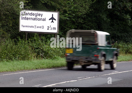 landrover driving past a spoof road sign indicating that small welsh village Llandegley has international airport Stock Photo