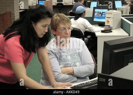Asian American female helps another female with computer at Lansing community college Stock Photo