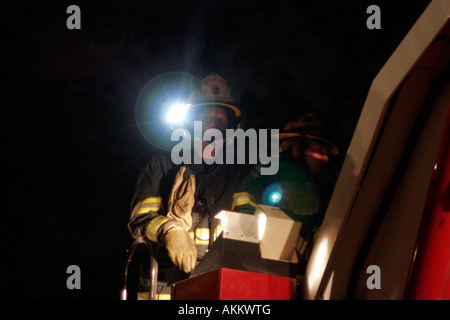 Two firefighters at the controls of a ladder truck at night with their flashlights on Stock Photo