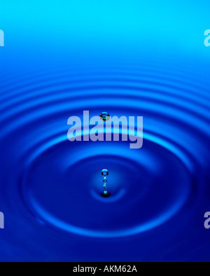 water droplets hitting surface of blue water with circular ripples Stock Photo