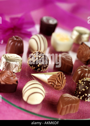 A COLLECTION OF FINE QUALITY BELGIAN CHOCOLATES ON A GLASS AND PINK BACKGROUND Stock Photo