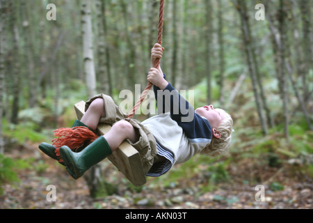A young boy on a rope swing in some woodland Stock Photo