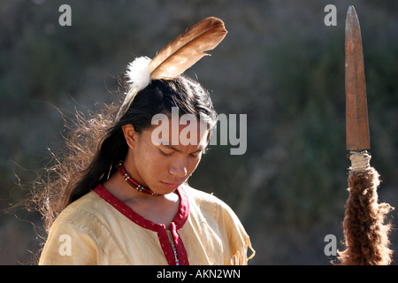 A Native American Indian boy wearing a feather standing holding a spear with buffalo hide on it Stock Photo
