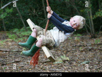 A young boy on a rope swing in some woodland Stock Photo