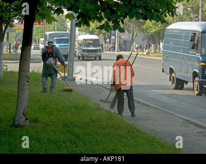 Street cleaners using powered strimmer and hand tools on Sovetskaya Street in Gomel Belarus Stock Photo