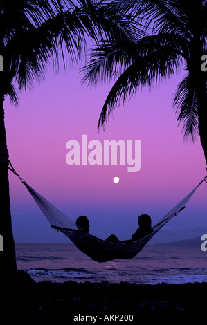 A couple in a hammock enjoy a full moon setting on the West side of Maui Stock Photo