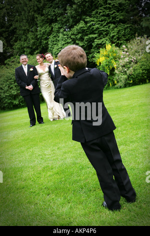 Young boy in suit takes a photo of a bride and groom with Father at a wedding in the UK outside summer garden lawn grass green Stock Photo