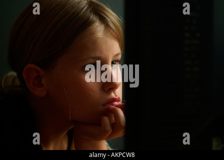 Young girl sitting at a computer desk using a computer and looking at a computer monitor screen while she works. Stock Photo
