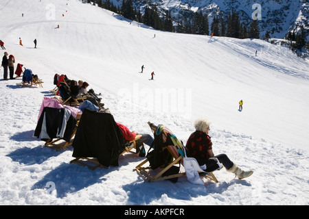 people seated in deck chairs watching the skiing on the slopes Stock Photo