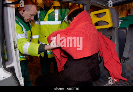 Paramedics helping a young woman wrapped in red blanket into an ambulance after she fell on St Marys Street Cardiff South Wales Stock Photo