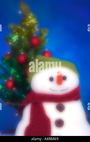 Artificial snowman with a big smile in front of a green artificial Christmas tree decorated with red and green round ornaments Stock Photo