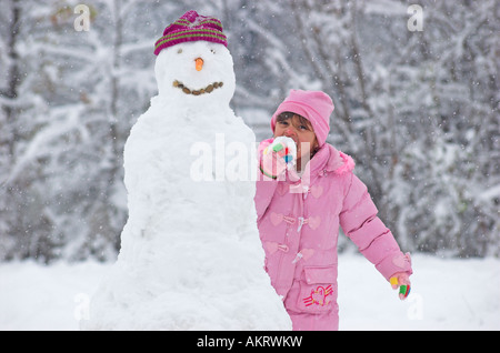 Girl standing next to snowman tasting snowball Stock Photo