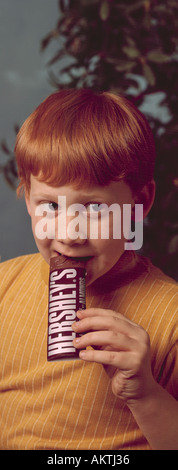 young freckle freckled face red head headed boy 5 6 7 eating Hershey chocolate candy bar Stock Photo