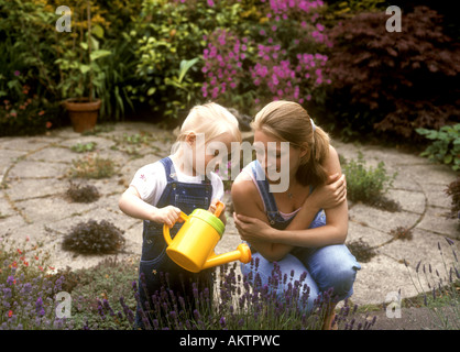 Toddler old with her mother using a watering can to water lavender plants in the garden Stock Photo