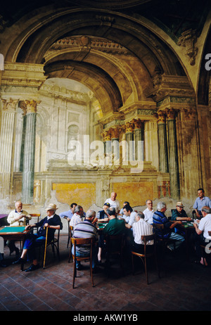Sorrento. Italy. A group of Italian men gather to play cards against a backdrop of fading frescoes in the Sedil Dominova. Stock Photo