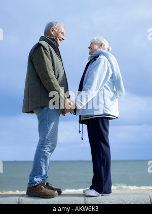 Senior couple standing on wall by water, holding hands Stock Photo