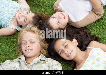 Smiling Pre-teen Children Lying on backs in circle on Grass, overhead view Stock Photo