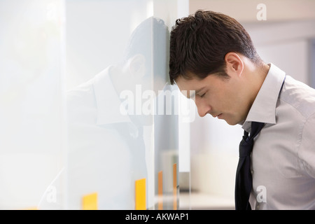 Unhappy Businessman resting head against office wall, side view