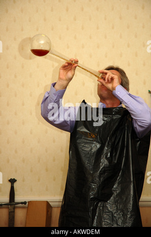 Young man drinking a yard of ale with plastic bin bag over his clothes to catch the spillage Stock Photo