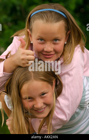 Young blond girl giving the 'thumbs-up' sign while getting a piggyback ride from her sister. Stock Photo