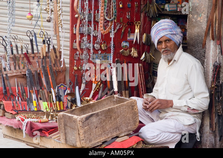 A merchant sells knives, scissors, and other goods from his tiny stall in Girdikot Market, Jodhpur, India. Stock Photo