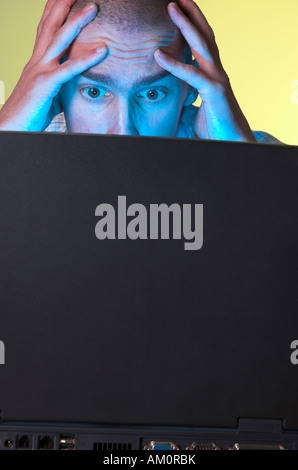Computer user having a bad day with tech problems online. His face illuminated by the screen of his laptop has a worried frustrated expression. Stock Photo